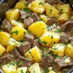 Slow cooker steak and cheddar potato casserole in white bowl with melted cheese and fresh parsley garnish