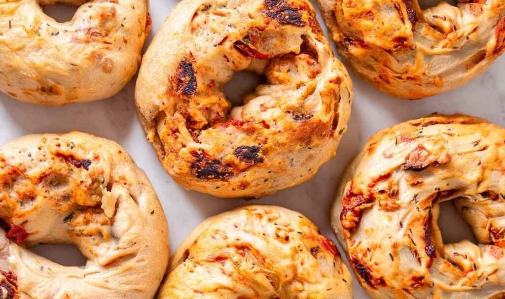 Sourdough bagels with sun-dried tomatoes and herbs on cooling rack with golden brown crust