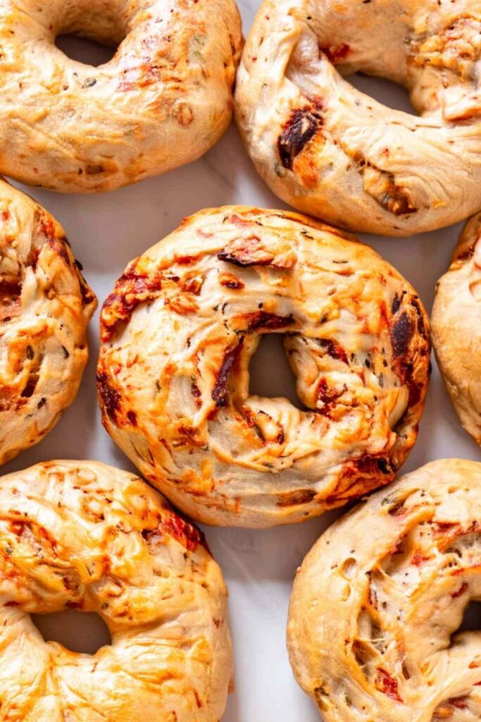 Sourdough bagels with sun-dried tomatoes and herbs on cooling rack with golden brown crust