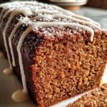 Sliced spiced gingerbread loaf with vanilla glaze drizzled on top on white serving plate