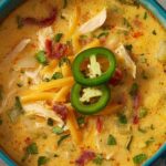 Bowl of Spicy Jalapeno Popper Chicken Soup topped with sour cream and fresh jalapeno slices