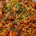 Sticky garlic chicken noodles in a white bowl with sesame seeds and green onions on top