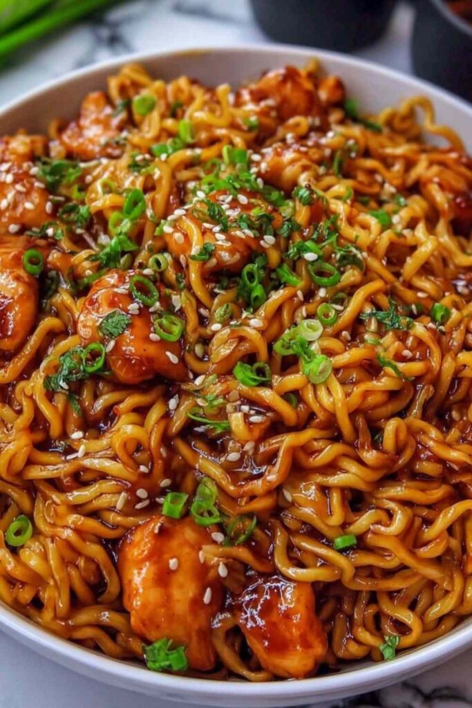 Sticky garlic chicken noodles in a white bowl with sesame seeds and green onions on top