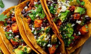 Sweet potato and black bean tacos on a plate with fresh cilantro lime and avocado toppings