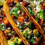 Sweet potato and black bean tacos on a plate with fresh cilantro lime and avocado toppings