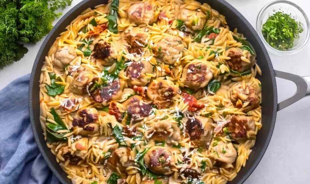 Tuscan chicken meatballs and orzo in creamy tomato sauce with spinach in a skillet