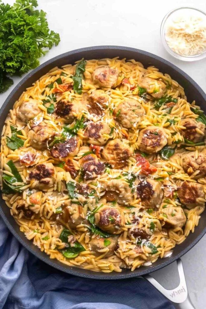 Tuscan chicken meatballs and orzo in creamy tomato sauce with spinach in a skillet