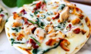 Tuscan Garlic Chicken Pita Pizzas topped with melted cheese, spinach, and sun-dried tomatoes on baking sheet