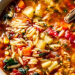 Vegetable orzo soup in white bowl with fresh parsley and parmesan cheese