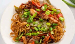 Chicken ramen stir fry in a wok with colorful vegetables and chopsticks