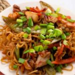 Chicken ramen stir fry in a wok with colorful vegetables and chopsticks