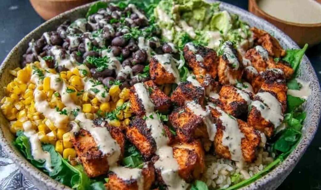 Chipotle chicken bowl with seasoned chicken, brown rice, black beans, corn, avocado, and lime wedges