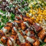 Chipotle chicken bowl with seasoned chicken, brown rice, black beans, corn, avocado, and lime wedges