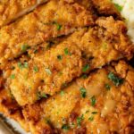 Golden crispy Country Fried Chicken on a white plate with mashed potatoes and gravy