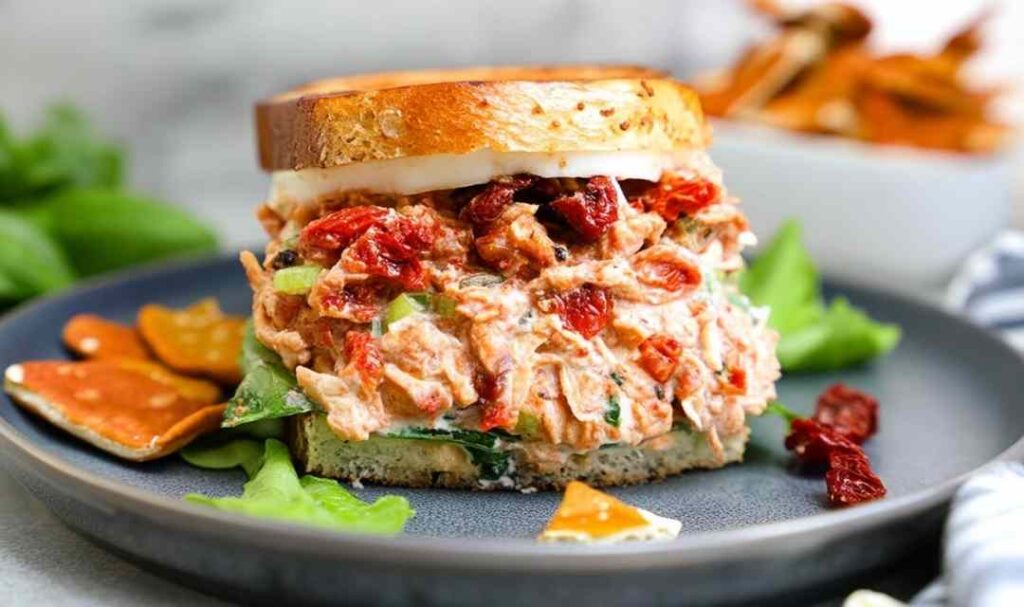 Sun-dried tomato chicken salad in a white bowl with fresh basil garnish