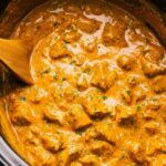 Crockpot butter chicken served over basmati rice with warm naan and fresh cilantro garnish
