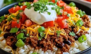 Easy Taco Rice Bowl (Quick and Flavorful Dinner Idea!) Easy taco rice bowl with seasoned ground beef, shredded cheddar, fresh lettuce, diced tomatoes, and sour cream in a white bowl