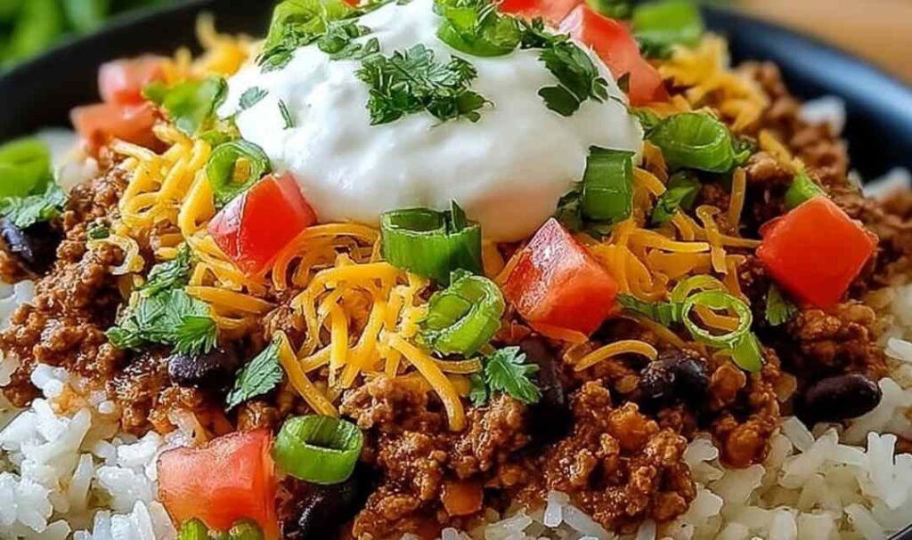 Easy taco rice bowl with seasoned ground beef, shredded cheddar, fresh lettuce, diced tomatoes, and sour cream in a white bowl