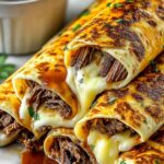 French Dip Tortilla Roll Ups on white plate with bowl of au jus dipping sauce