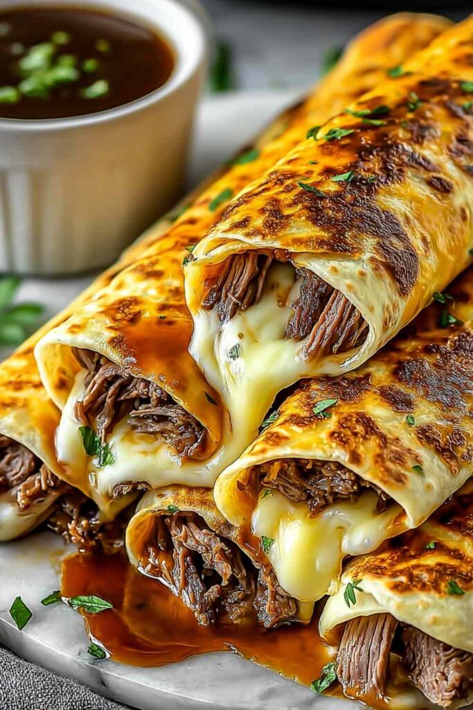 French Dip Tortilla Roll Ups on white plate with bowl of au jus dipping sauce