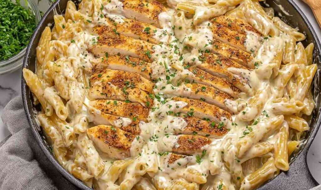 Garlic parmesan chicken pasta on a white plate with creamy sauce and fresh parsley garnish