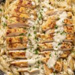 Garlic parmesan chicken pasta on a white plate with creamy sauce and fresh parsley garnish