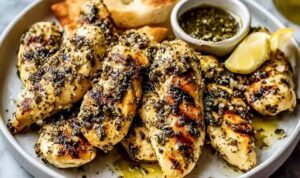 Greek chicken tenders on white plate with lemon wedges and fresh herbs