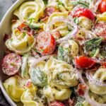 Fresh grinder tortellini salad with salami, pepperoni, provolone, cherry tomatoes, and zesty Italian dressing in a large white bowl