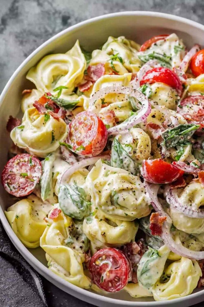 Fresh grinder tortellini salad with salami, pepperoni, provolone, cherry tomatoes, and zesty Italian dressing in a large white bowl