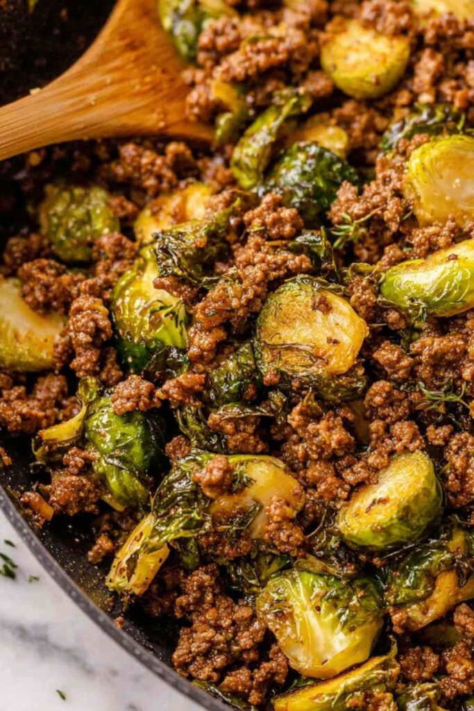 Ground beef and brussels sprouts in skillet with sweet chili sauce and sesame seeds