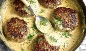 Hamburger steak in creamy dill sauce served over mashed potatoes in a cast iron skillet