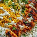 Healthy street corn chicken rice bowl with juicy seasoned chicken, creamy elote corn, black beans, and fresh avocado in a white bowl