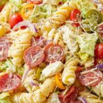 Italian grinder pasta salad with rotini, pepperoni, ham, provolone, and banana peppers in a white bowl