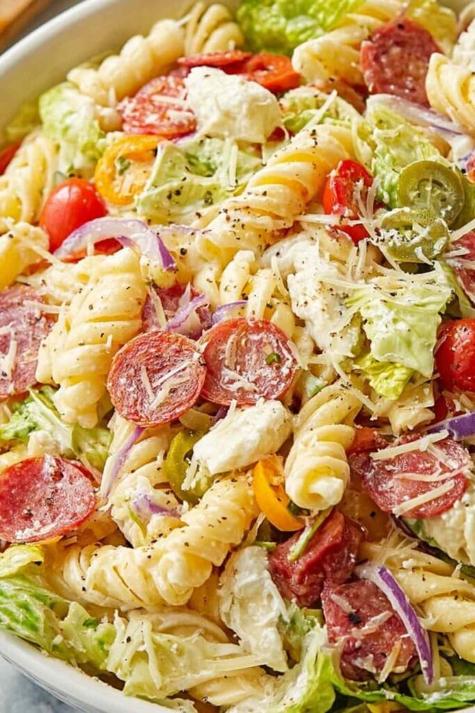 Italian grinder pasta salad with rotini, pepperoni, ham, provolone, and banana peppers in a white bowl