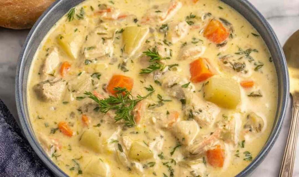 Leftover Turkey Soup 5 A ceramic bowl of leftover turkey soup with egg noodles, carrots, celery, and fresh parsley garnish on a wooden table