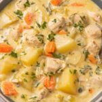A ceramic bowl of leftover turkey soup with egg noodles, carrots, celery, and fresh parsley garnish on a wooden table