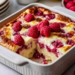 Lemon raspberry cottage cheese bake in white baking dish with golden top and fresh raspberries