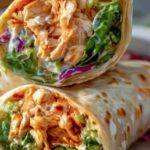 Spicy buffalo chicken wraps cut in half showing shredded chicken, lettuce, and carrots inside flour tortilla