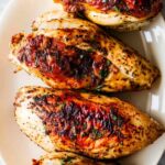 Golden roasted bone-in chicken breasts with crispy skin on white plate with roasted vegetables