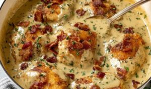 Smothered Chicken With Bacon Gravy Smothered chicken recipe with crispy bacon gravy in a cast iron skillet garnished with fresh parsley