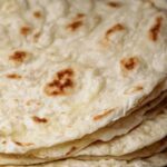 Soft sourdough discard tortillas stacked on plate with visible brown spots