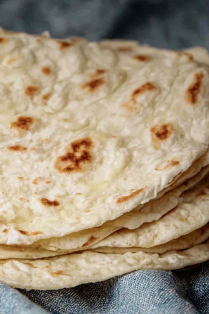 Soft sourdough discard tortillas stacked on plate with visible brown spots
