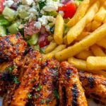 Spicy grilled chicken wings with fries and Greek salad served on a platter