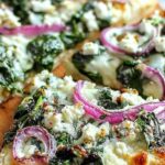 Spinach and feta flatbread pizza with melted cheese and sun-dried tomatoes on baking sheet