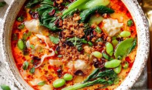 Thai Coconut Dumpling Soup in a white bowl with fresh cilantro, basil, and red bell pepper