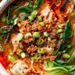 Thai Coconut Dumpling Soup in a white bowl with fresh cilantro, basil, and red bell pepper
