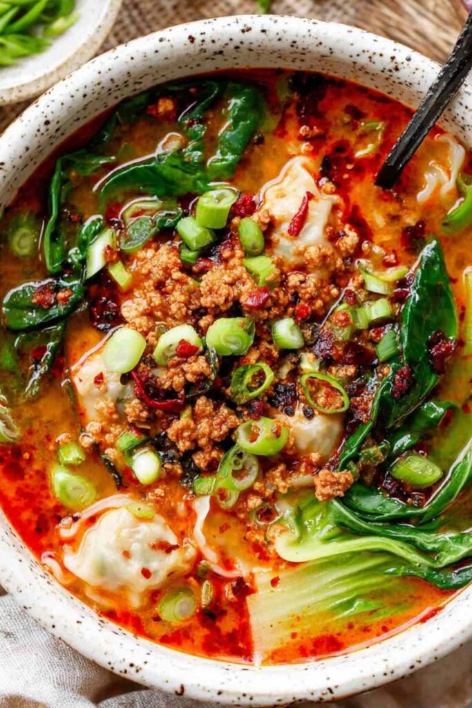 Thai Coconut Dumpling Soup in a white bowl with fresh cilantro, basil, and red bell pepper