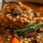 A bowl of hearty beef barley soup with tender beef chunks, pearl barley, carrots, and celery in a rich savory broth garnished with fresh parsley