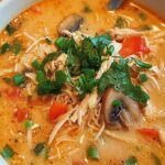 Bowl of Thai chicken soup with coconut milk broth, fresh cilantro, and green onions on a wooden table