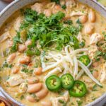 A bowl of Cajun white chicken chili topped with shredded cheese, sliced green onions, and sour cream